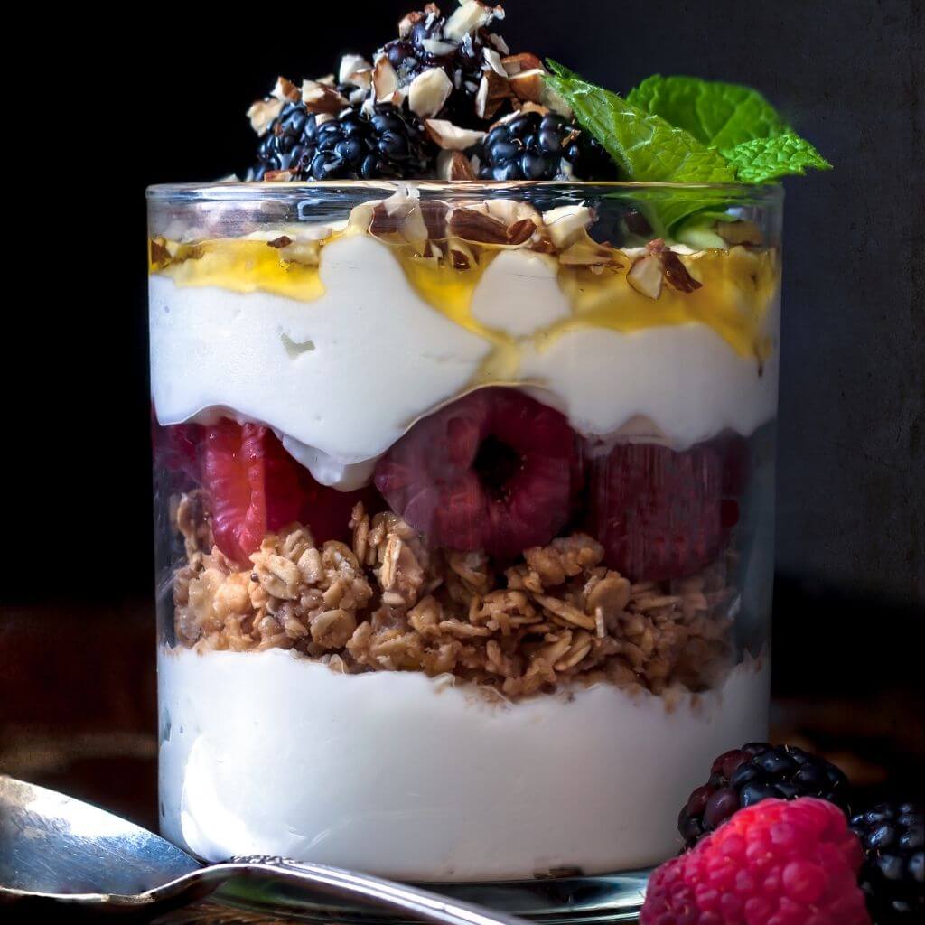 Glass of Honey and Yogurt Parfait with layers of yogurt, granola, and honey, garnished with sliced strawberries.